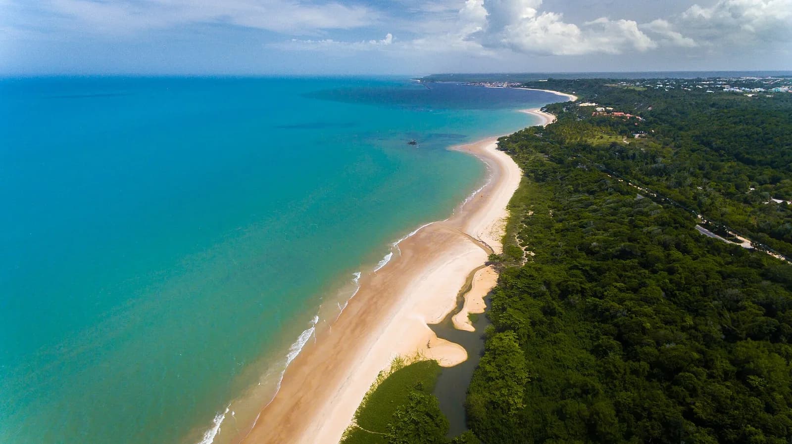 Vista aérea da Praia de Mundaí, em Porto Seguro, com faixa longa de areia clara entre o mar turquesa e a mata